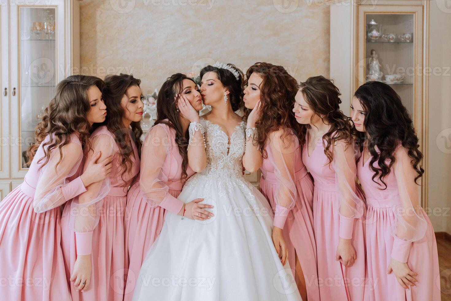 portret van de bruid met haar vrienden in de kamer. een brunette bruid in een lang wit jurk en haar vrienden in roze jurken zijn glimlachen en gelukkig. jong meisjes. foto
