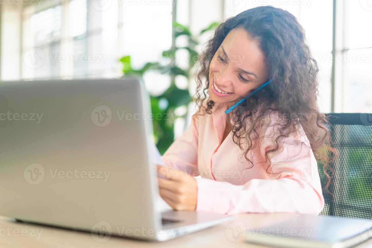 Latijnse vrouw die met telefoon aan werkruimte werkt foto