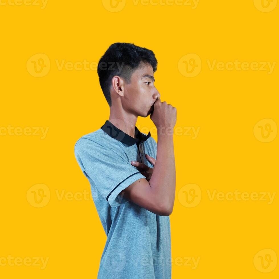 een Aziatisch Mens is aan het bedekken zijn mond met zijn handen gebalde in vuisten Holding zijn borst, geïsoleerd Aan een geel achtergrond foto