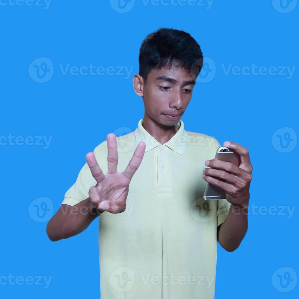 opgewonden Aziatisch Mens vervelend geel t-shirt geven aantal 12345 hand- gebaar. blauw achtergrond foto