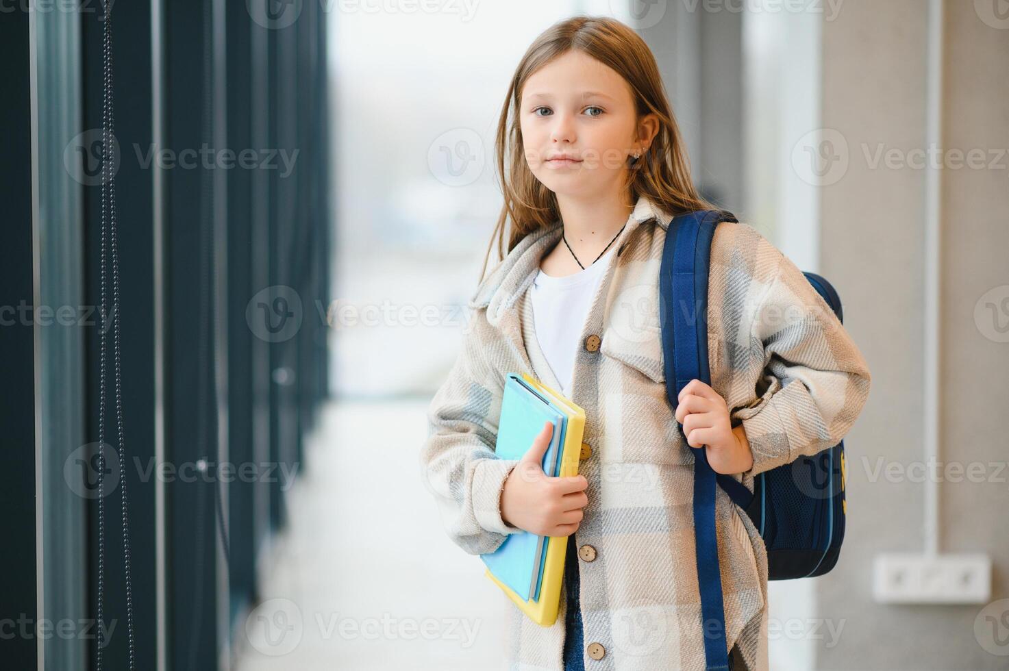 weinig mooi school- meisje staand tussen gang Bij school, Holding aantekeningen Bij handen. grappig en gelukkig meisje glimlachen Bij camera, resting na lessen Aan primair school- foto