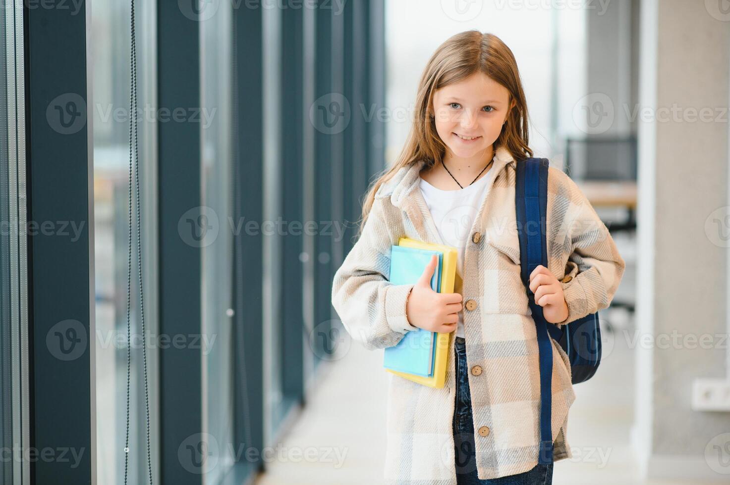 weinig mooi school- meisje staand tussen gang Bij school, Holding aantekeningen Bij handen. grappig en gelukkig meisje glimlachen Bij camera, resting na lessen Aan primair school- foto