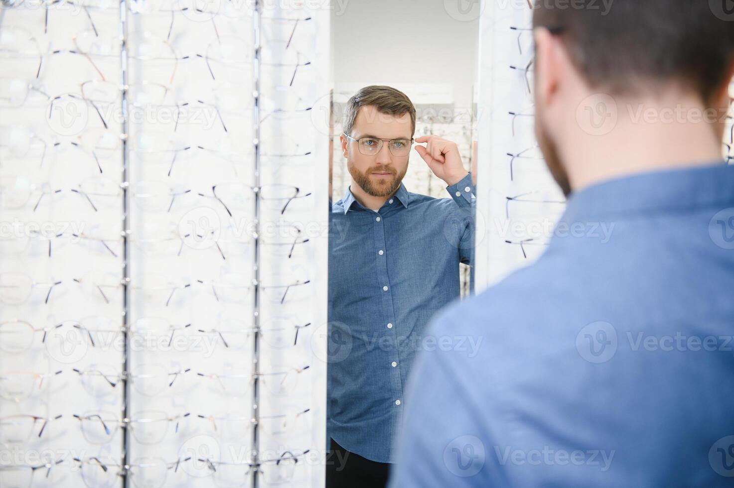 in optiek winkel. portret van mannetje cliënt Holding en vervelend verschillend bril, kiezen en proberen Aan nieuw bril Bij optisch op te slaan. Mens plukken kader voor visie correctie, detailopname. foto