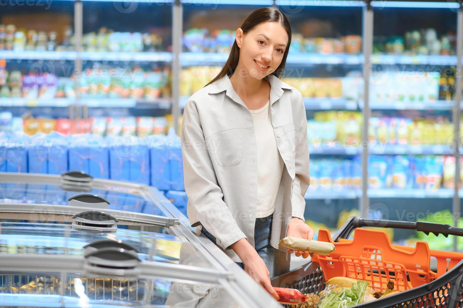 jong glimlachen gelukkig vrouw Jaren 20 in gewoontjes kleren boodschappen doen Bij supermarkt op te slaan met kruidenier kar foto