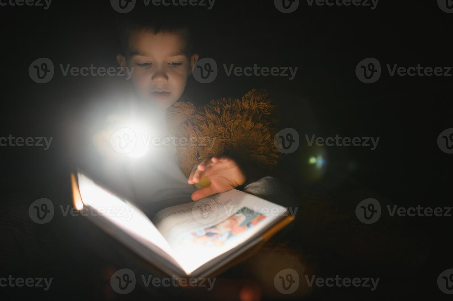 kind lezing boek in bed. kinderen lezen Bij nacht. weinig jongen met fee verhaal boeken in slaapkamer . onderwijs voor jong kinderen. bedtijd verhaal in de avond. schattig kind onder deken in donker kamer met lamp foto