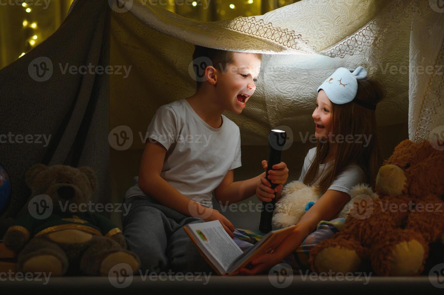 kinderen jongen en meisje spelen en schrikken elk andere met zaklamp in tent Bij nacht. foto