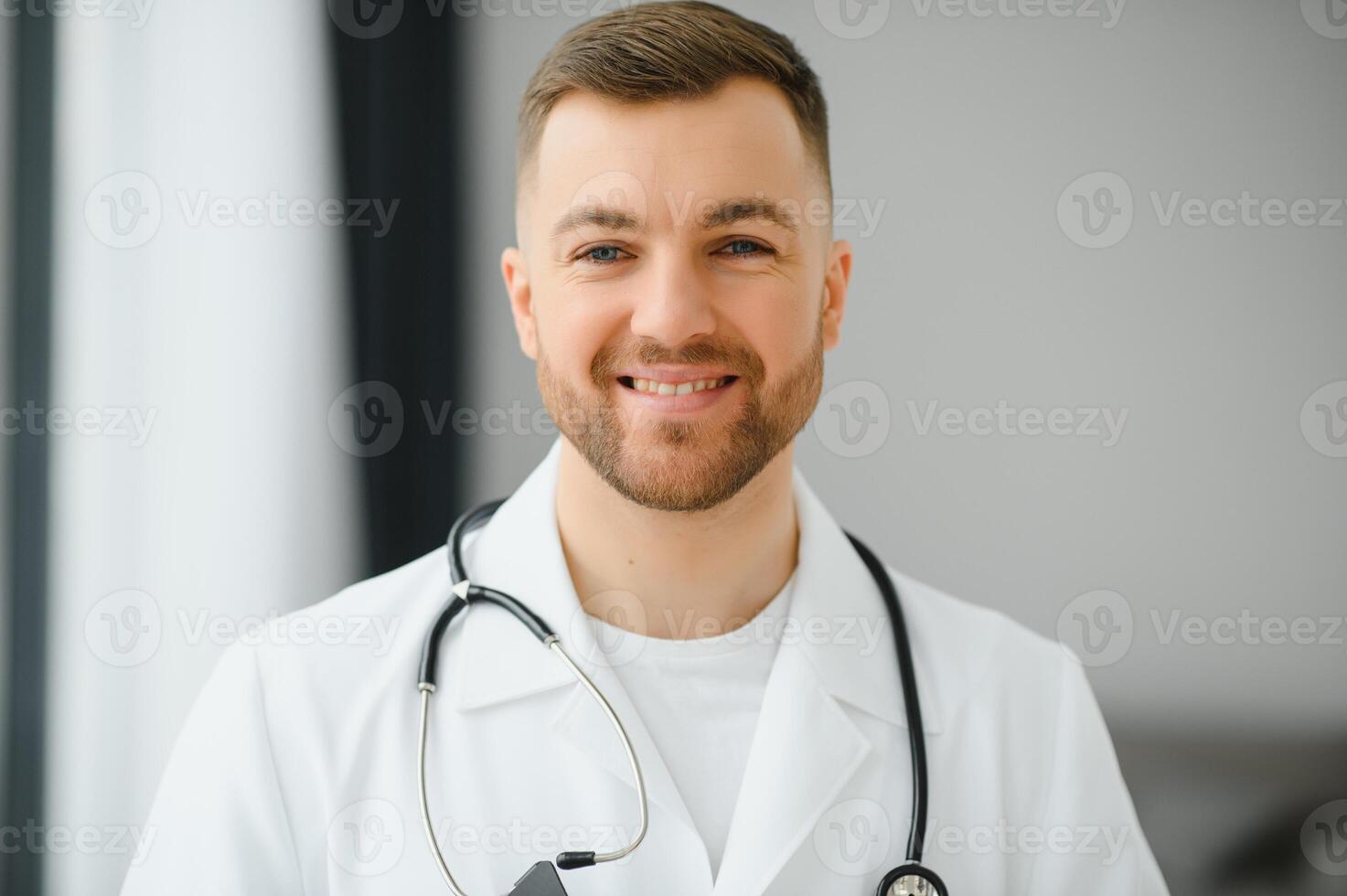 portret van knap jong dokter Aan ziekenhuis gang op zoek Bij camera, lachend. foto