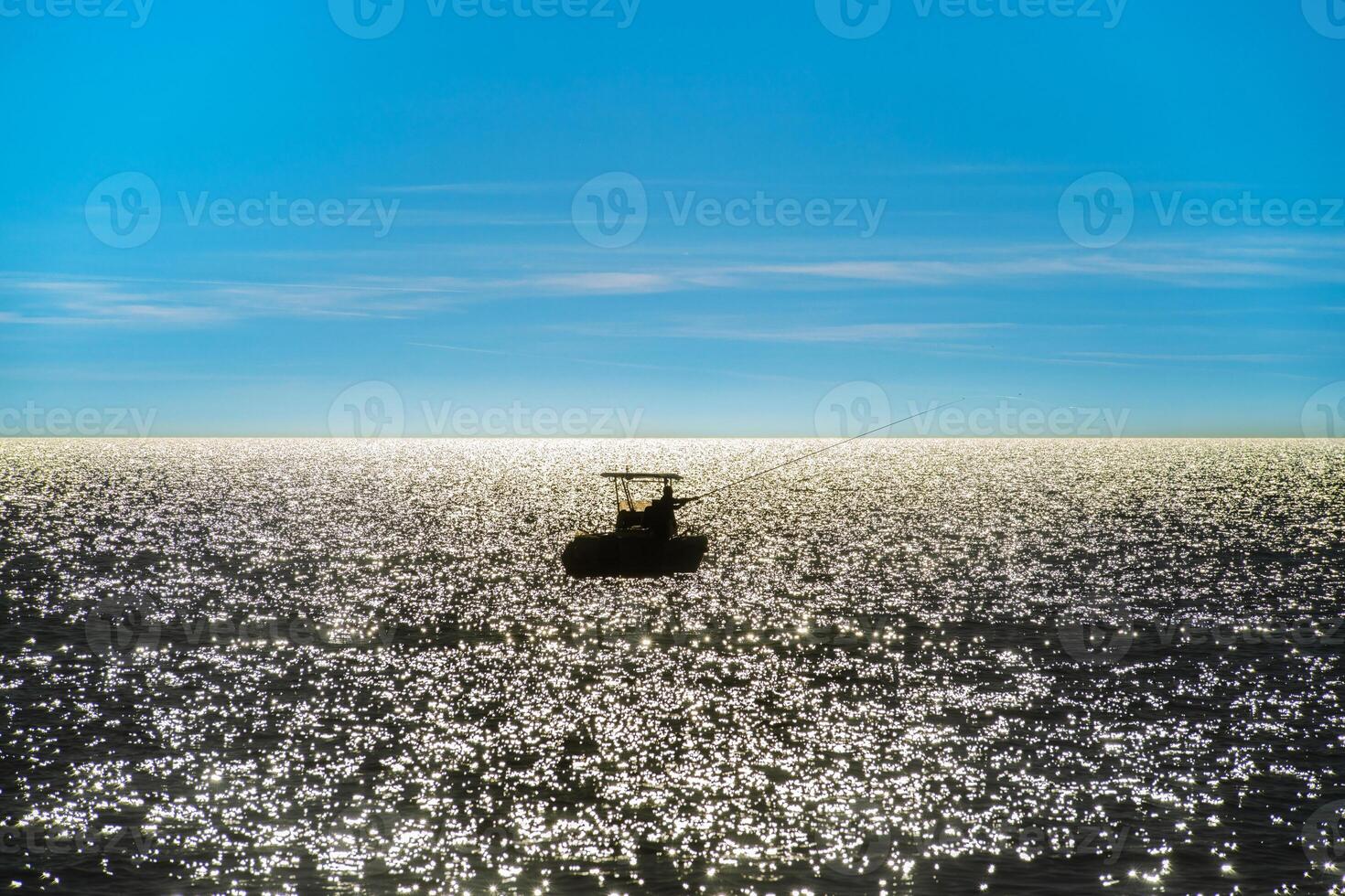 visser Aan een boot in achtergrondverlichting in de midden- van de zee foto