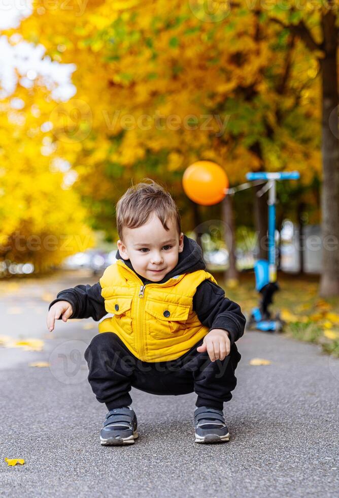 jong jongen in geel jasje spelen met bal. een vrolijk jong jongen vervelend een geel jasje blij Toneelstukken met zijn bal. foto