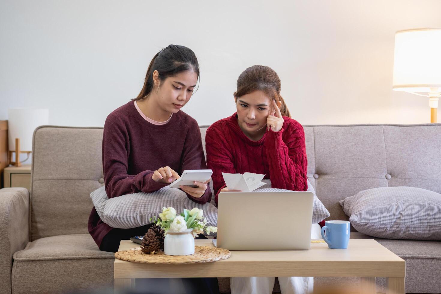 een jong Aziatisch vrouw zit Aan een sofa in haar huis, gevoel bezorgd en gefrustreerd over haar maandelijks uitgaven. divers nut rekeningen. foto