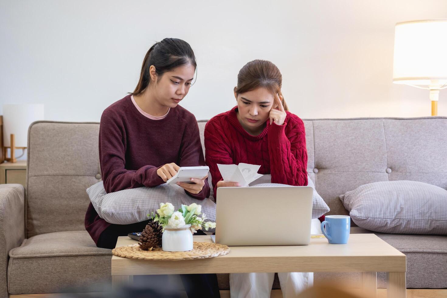 een jong Aziatisch vrouw zit Aan een sofa in haar huis, gevoel bezorgd en gefrustreerd over haar maandelijks uitgaven. divers nut rekeningen. foto