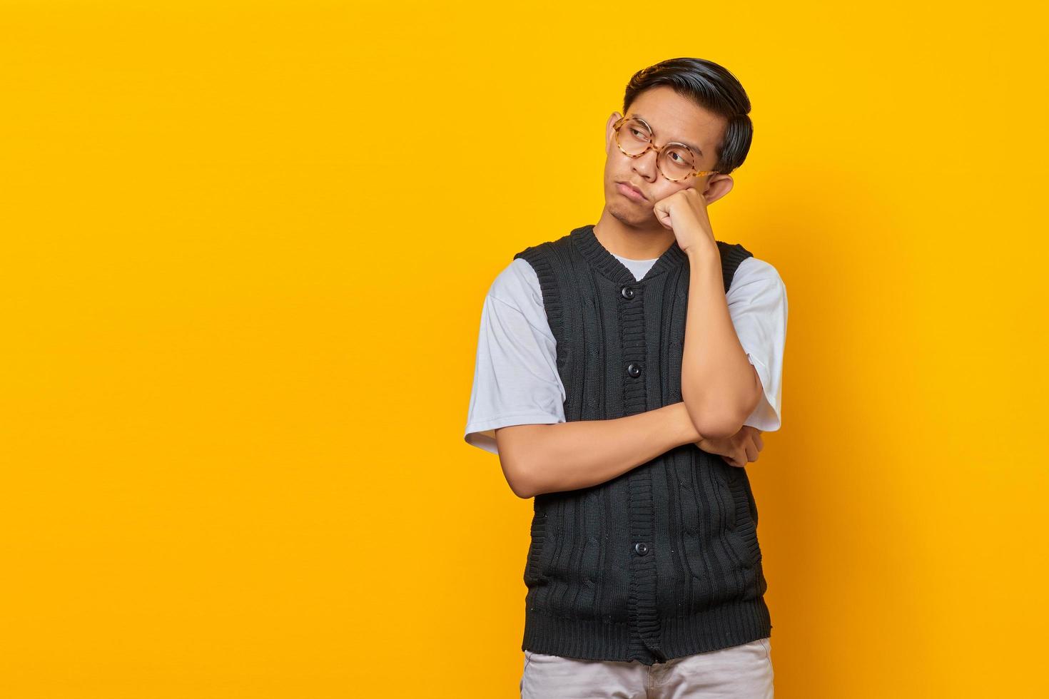 portret van een denkende aziatische man die de kin aanraakt en naar lege ruimte over gele achtergrond kijkt foto