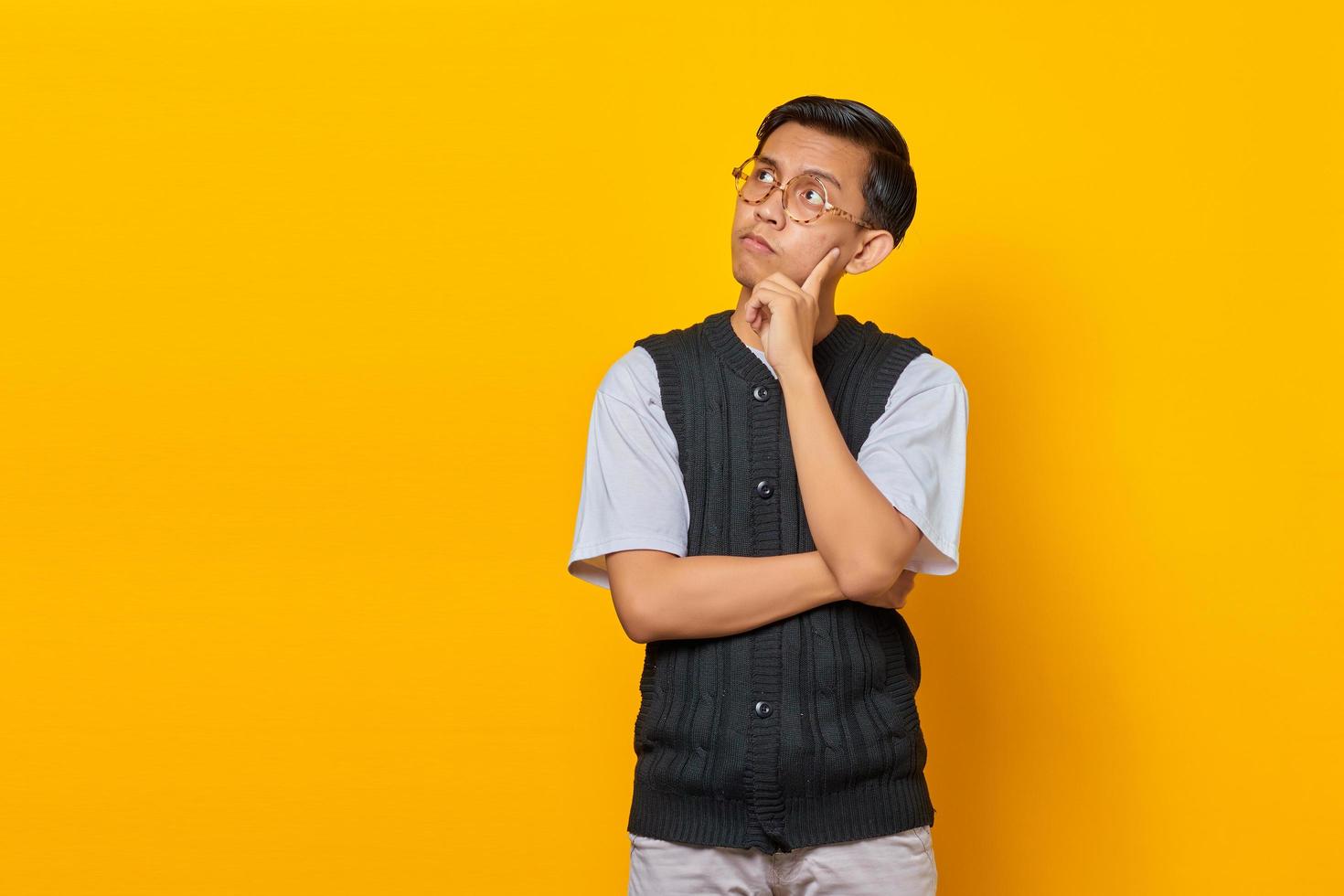 portret van een denkende aziatische man die de kin aanraakt en naar lege ruimte over gele achtergrond kijkt foto