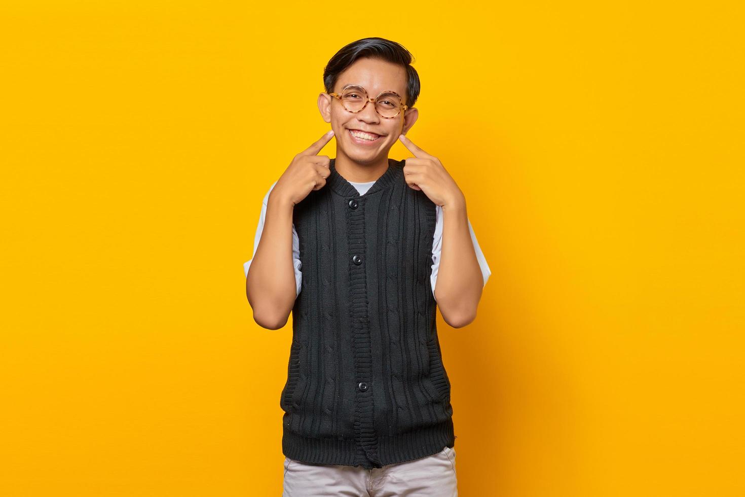 portret van glimlachende aziatische jonge man met twee vingers die kuiltjes wijzen over gele achtergrond foto