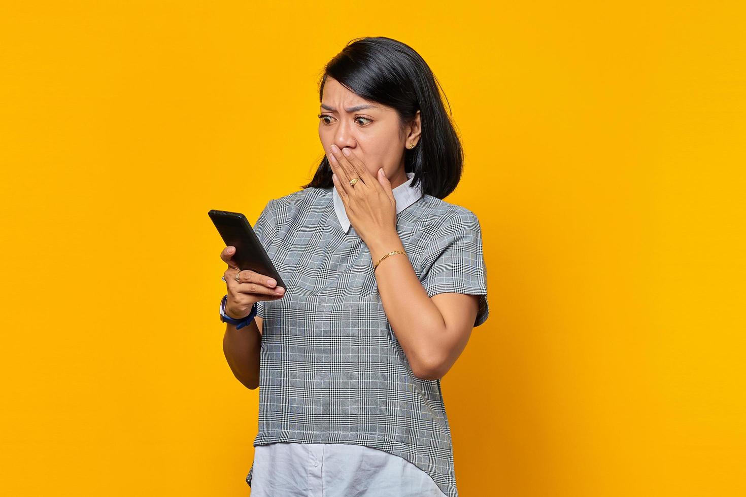 portret van een geschokte jonge aziatische vrouw die een smartphone vasthoudt en de mond bedekt met de hand? foto