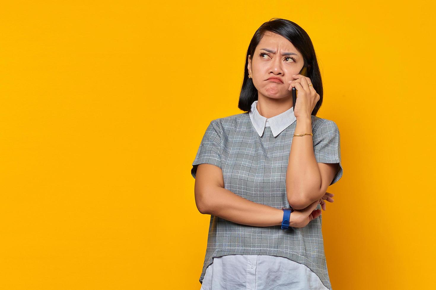 portret van geërgerde jonge aziatische vrouw die inkomende oproep op smartphone ontvangt en opzij kijkt op gele achtergrond foto