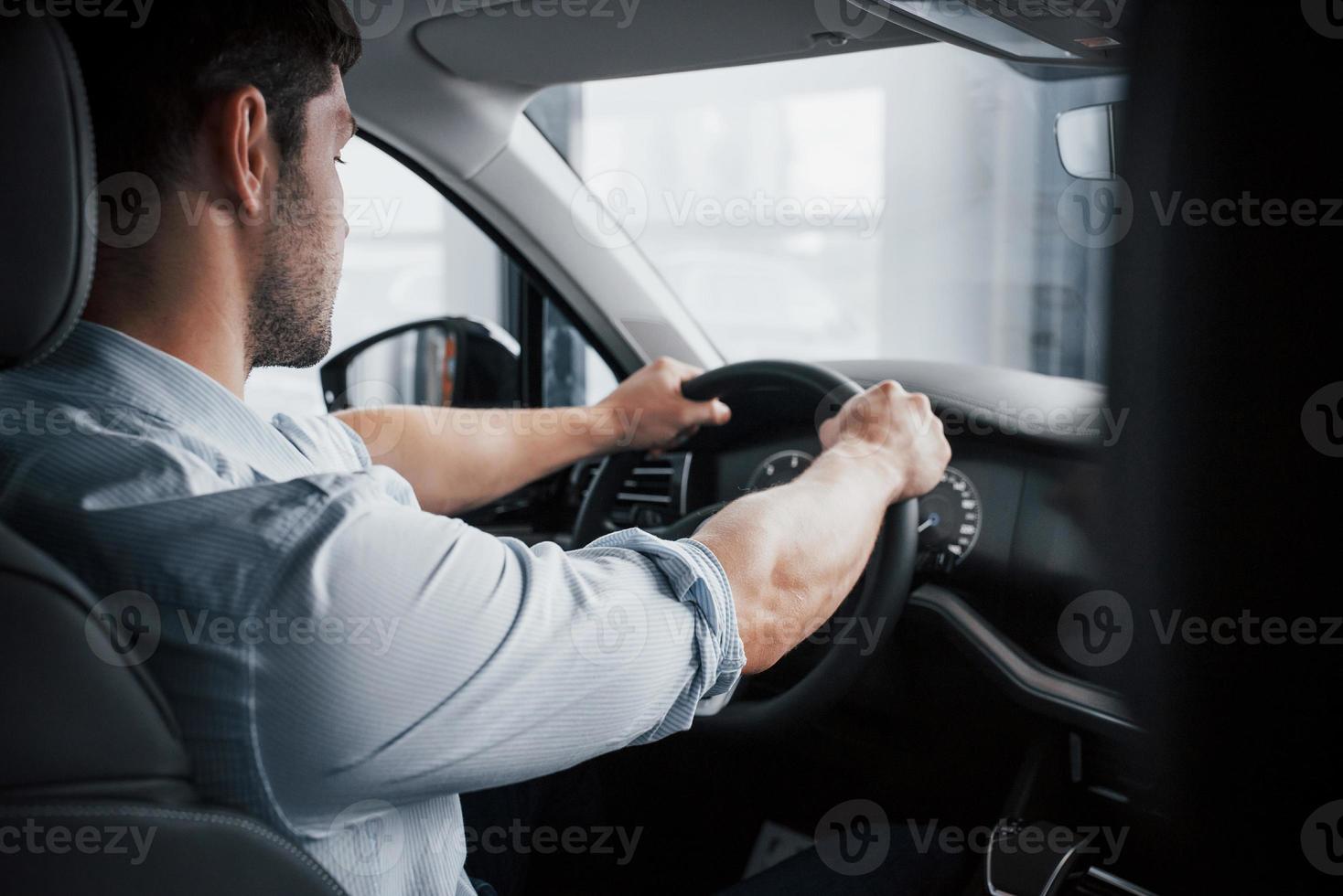 een jonge man zit in een pas gekochte auto en houdt zijn handen aan een roer. foto
