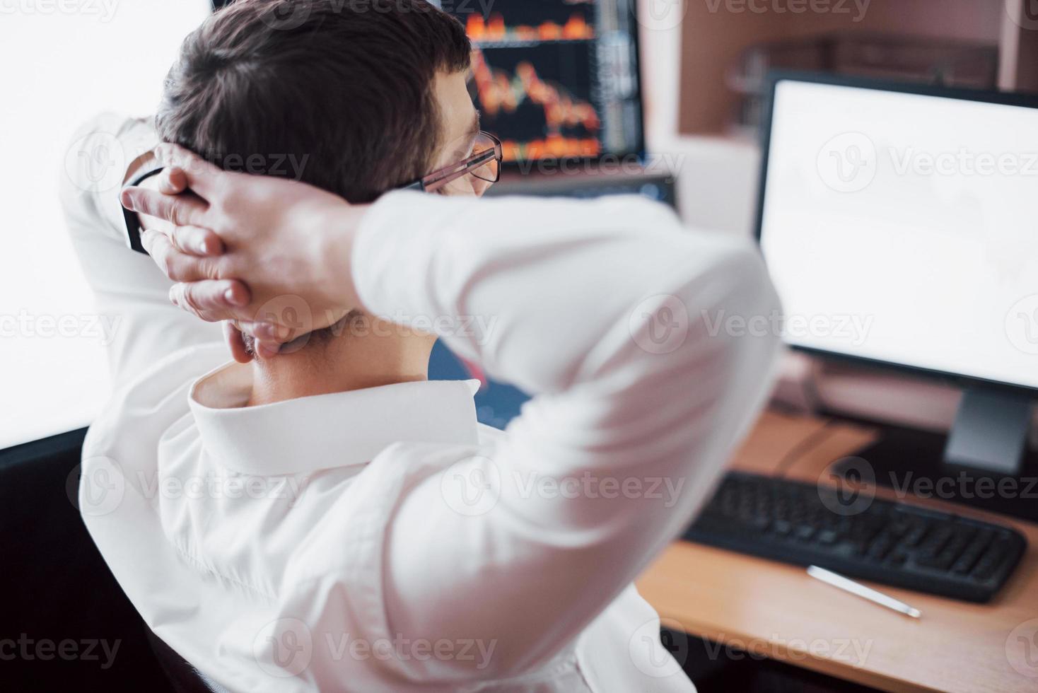 nieuwe benaderingen te ontwikkelen. achteraanzicht van een jonge man in vrijetijdskleding die de hand op de achterkant van het hoofd houdt en werkt terwijl hij aan het bureau zit in een creatief kantoor foto