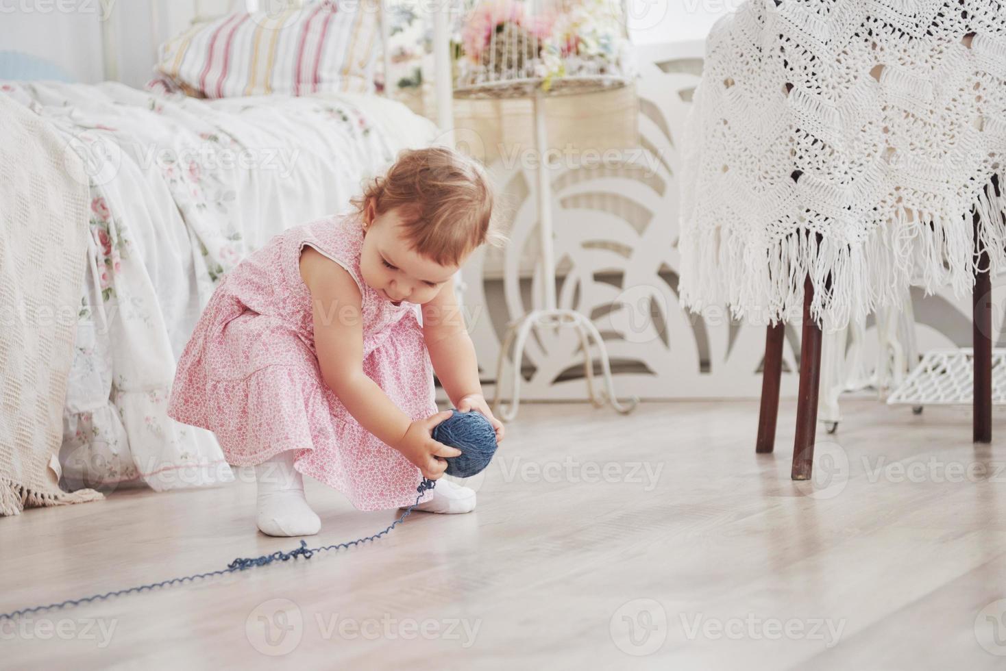 kindertijd concept. babymeisje in schattig jurkje spelen met gekleurde draad. witte vintage kinderkamer foto