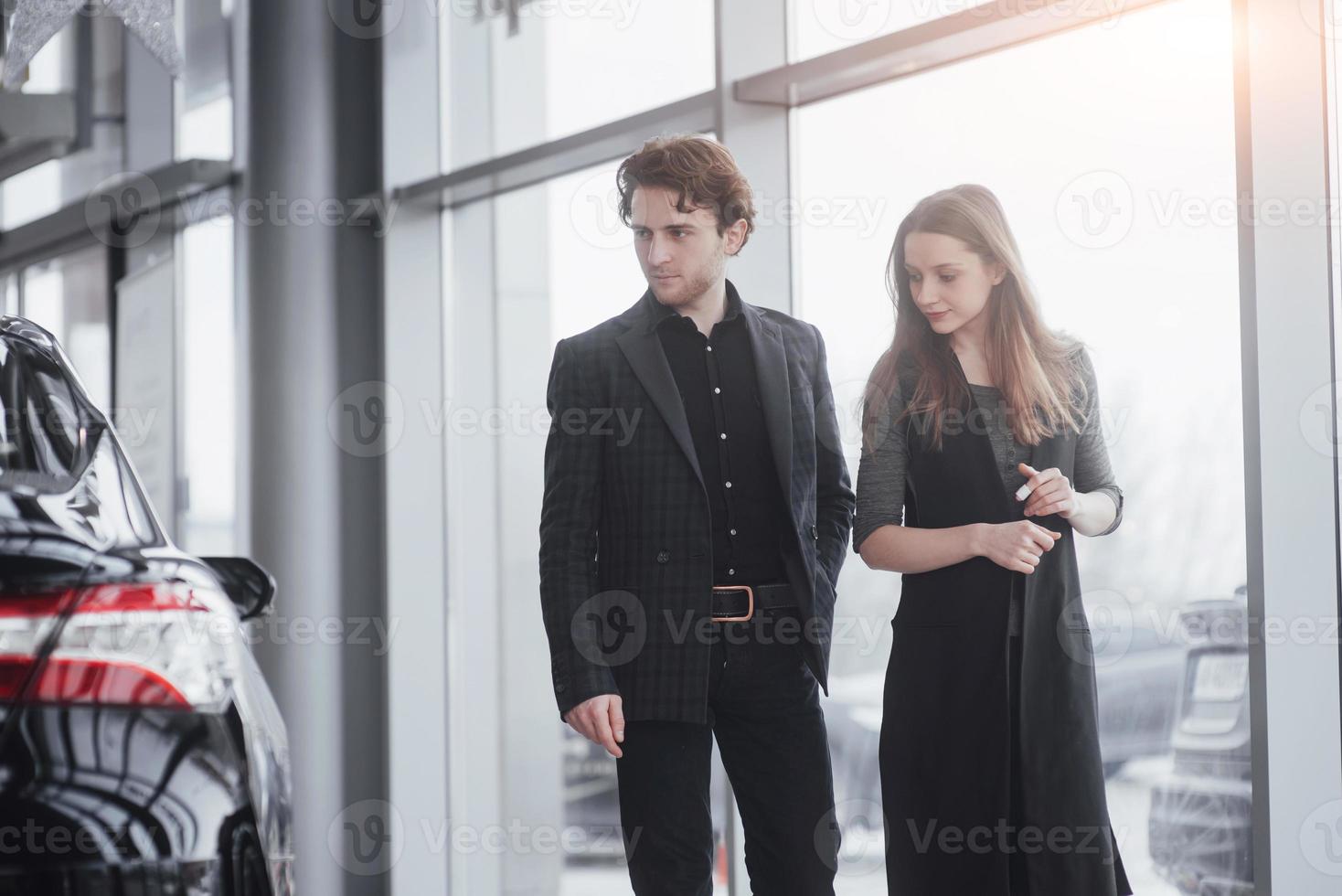 samen hun eerste auto kopen. hoge hoekmening van jonge autoverkoper die bij de dealer staat en de klanten vertelt over de kenmerken van de auto foto