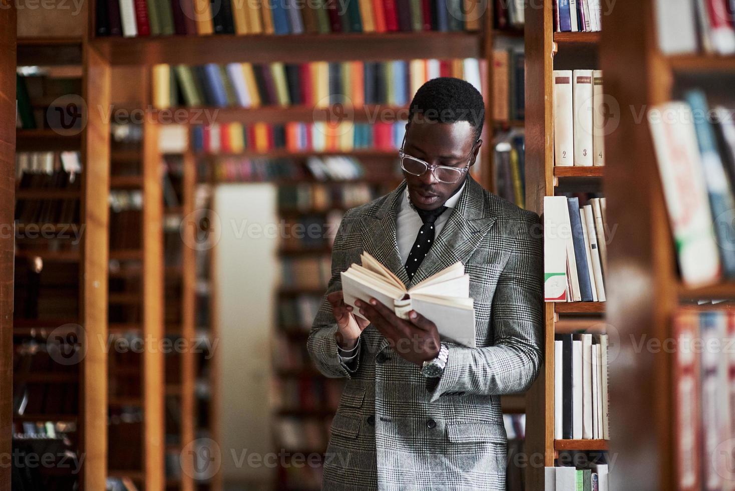 een Afro-Amerikaanse man in een pak die in een bibliotheek in de leeszaal staat. foto