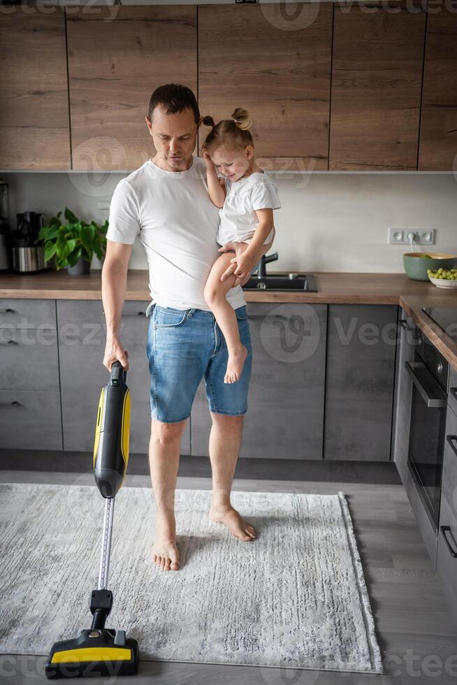 vader met zijn dochter Aan zijn handen stofzuigen de verdieping in de modern huis keuken foto