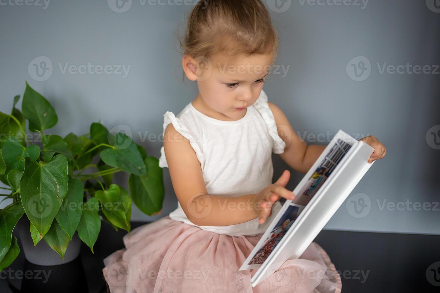 gelukkig schattig weinig meisje op zoek Bij foto's in album. gelukkig glimlachen dochter browsen door gedrukt familie album, op zoek Bij afbeeldingen. foto