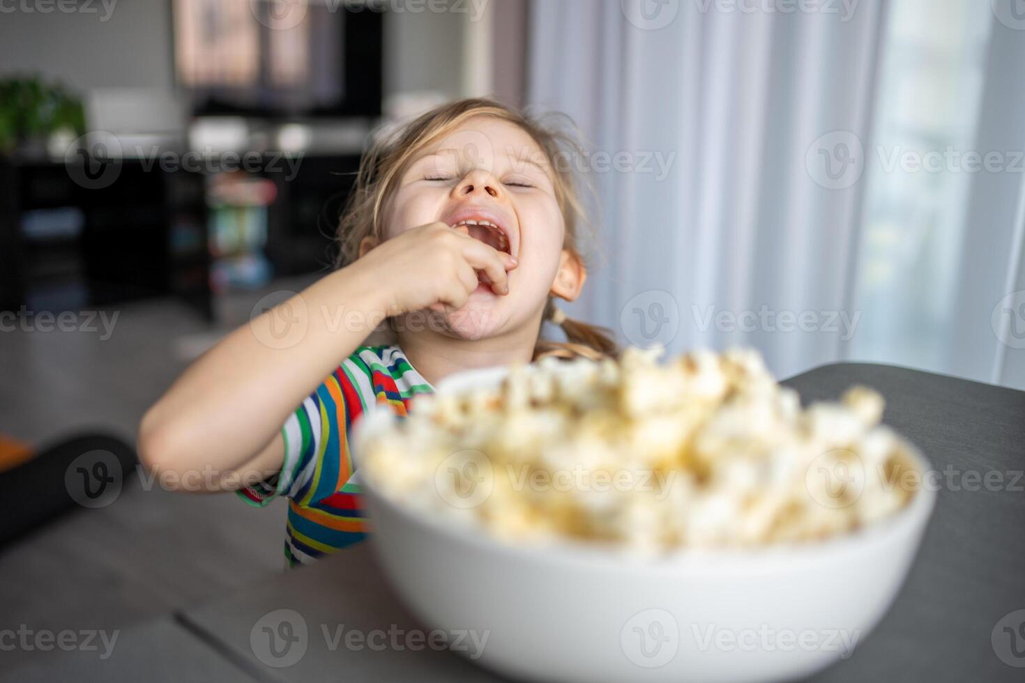 weinig meisje is aan het eten popcorn in huis keuken foto