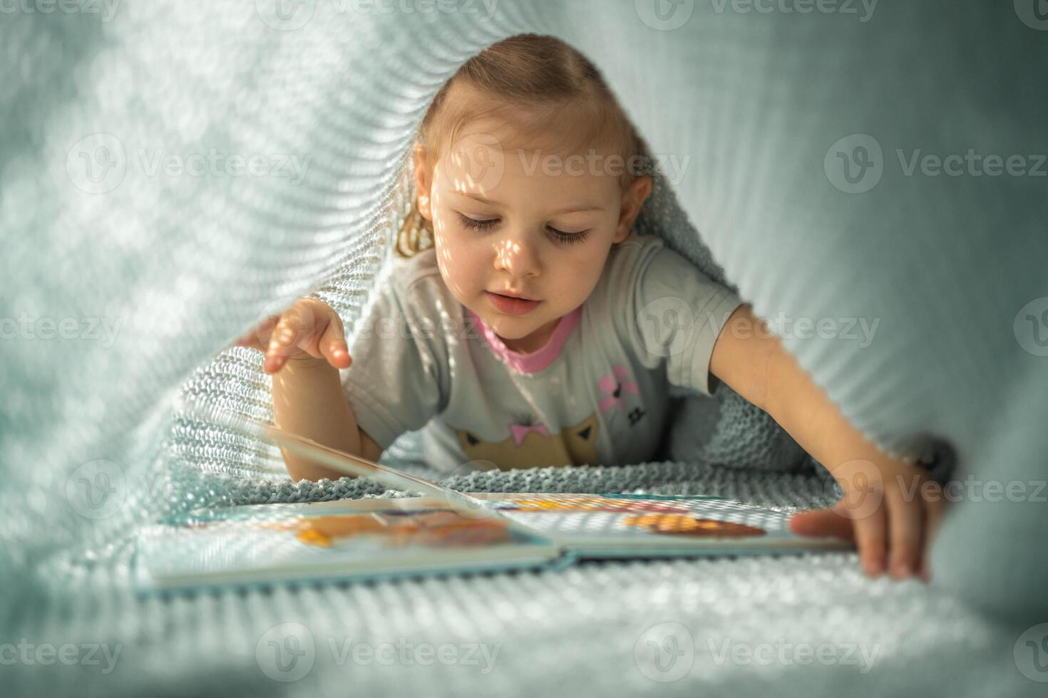 weinig meisje genieten van van recensie een boek onder blauw gebreid plaid in zonnig ochtend- foto
