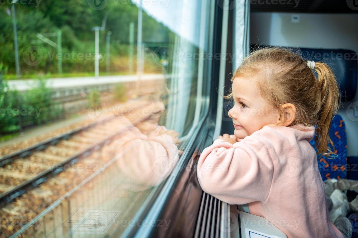 schattig weinig meisje op zoek uit trein venster buiten, terwijl het in beweging. op reis door spoorweg in Europa foto