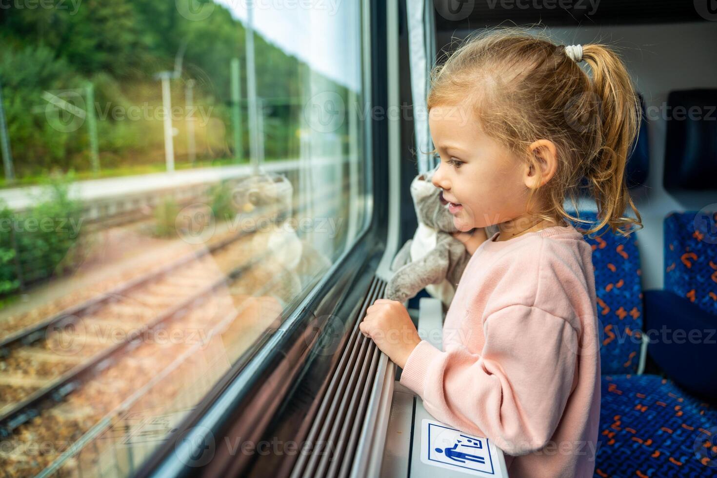 weinig meisje met speelgoed- op zoek uit trein venster buiten, terwijl het in beweging. op reis door spoorweg in Europa foto