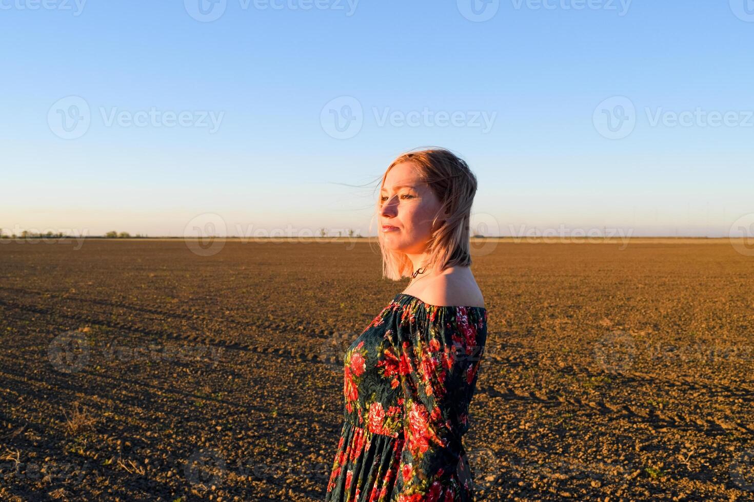 vrouw in een geploegd veld- in een rood Zwart jurk Aan een zonsondergang achtergrond. foto