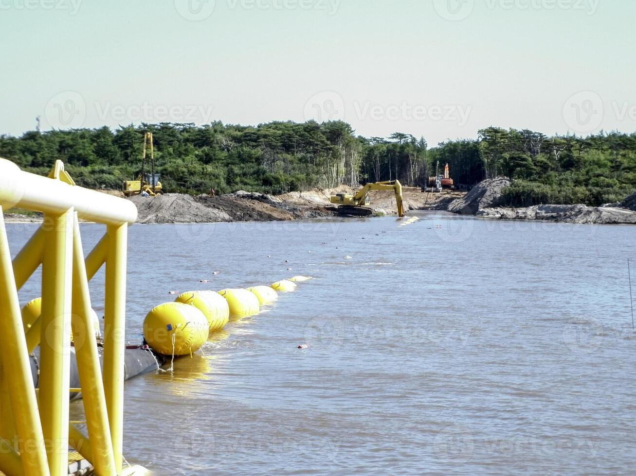 houdende van pijpen met Pijp ligging aak kraan in de buurt de oever. afdaling van de pijpleiding naar een bodem vermoeiend met de Pijp ligging schuit. installatie van de onderwater- gas- pijpleiding foto