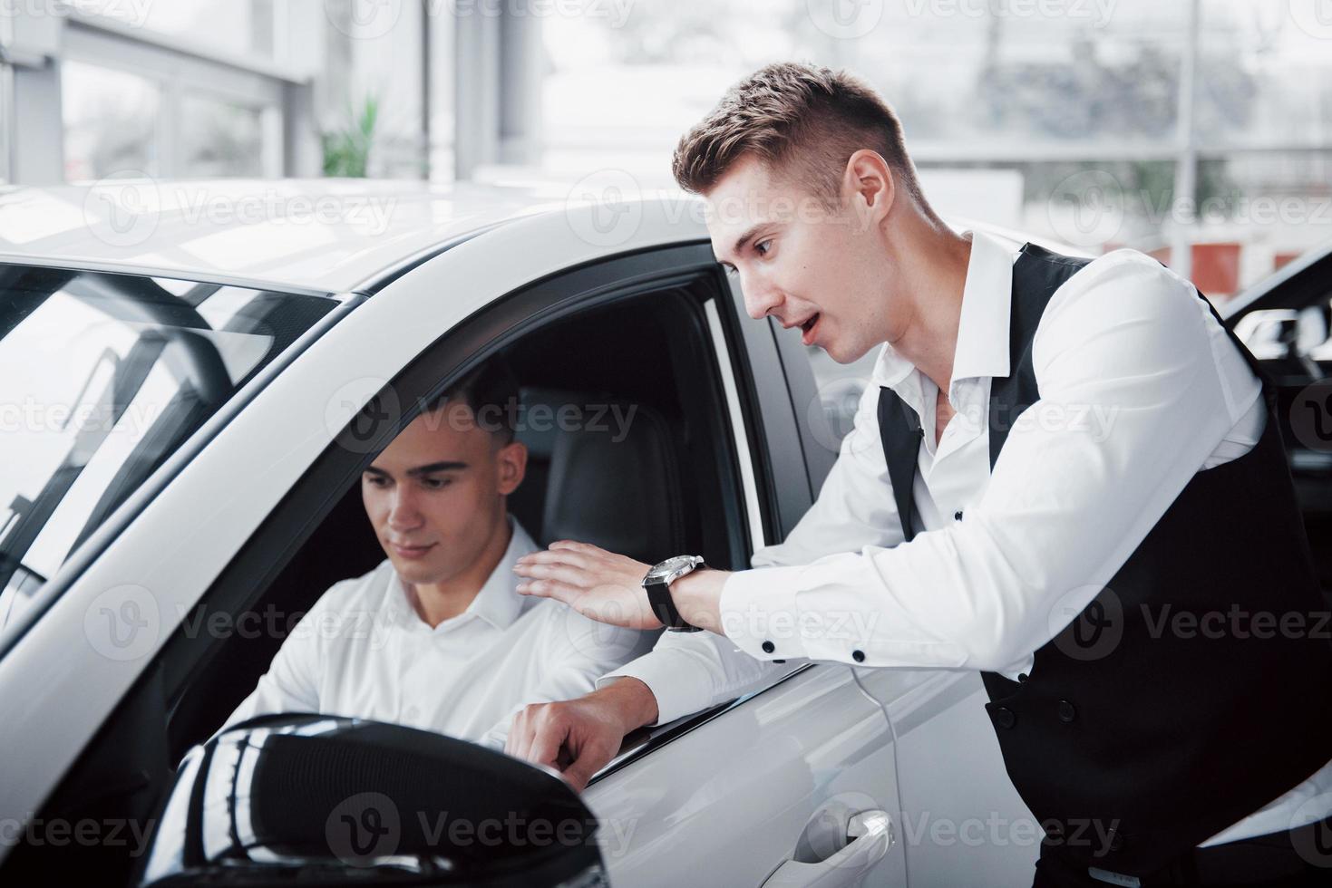 twee mannen staan in de showroom tegen auto's. close-up van een verkoopmanager in een pak die een auto aan een klant verkoopt. de verkoper geeft de sleutel aan de klant. foto