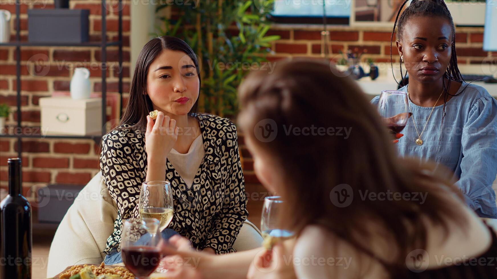 Aziatisch vrouw Bij appartement partij betalen aandacht naar interessant verhaal gedeeld door vriend terwijl aan het eten fijnproever kaas van vleeswaren schotel. bipoc gast luisteren naar groep van mensen chatten foto