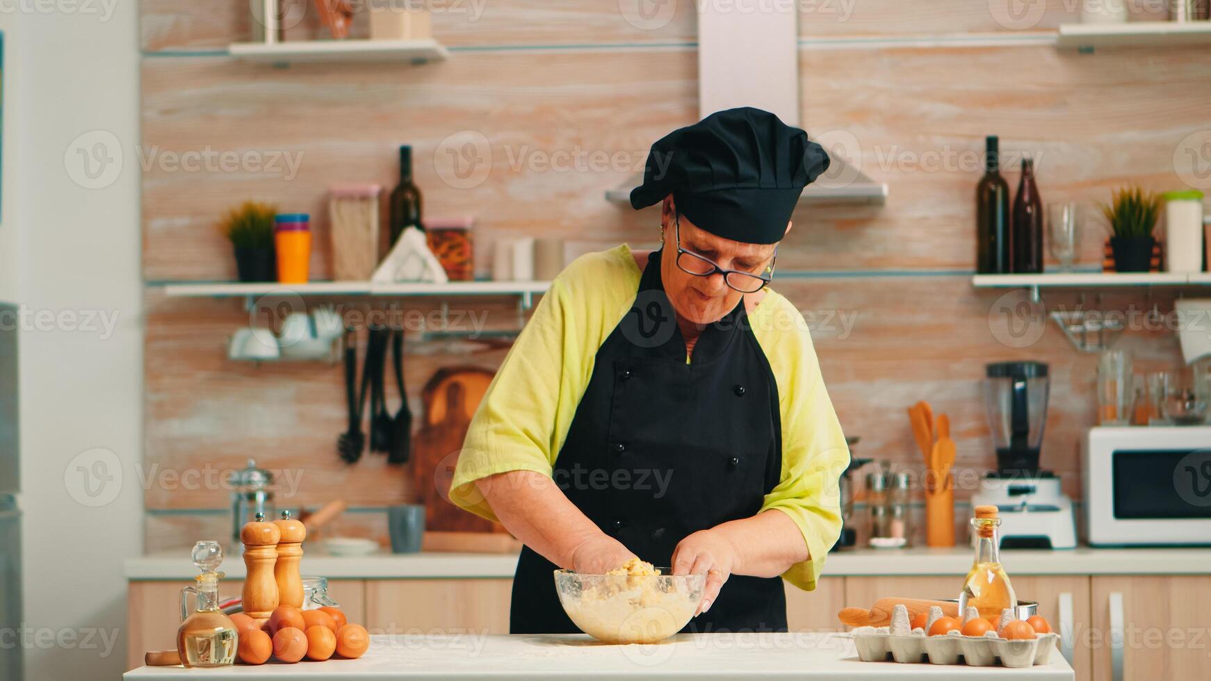 vrouw vervelend chef bot terwijl menging gebarsten eieren met meel in keuken terwijl voorbereidingen treffen voedsel in aansluiting op traditioneel recept. gepensioneerd ouderen bakker kneden in glas kom ingrediënten voor eigengemaakt taart foto