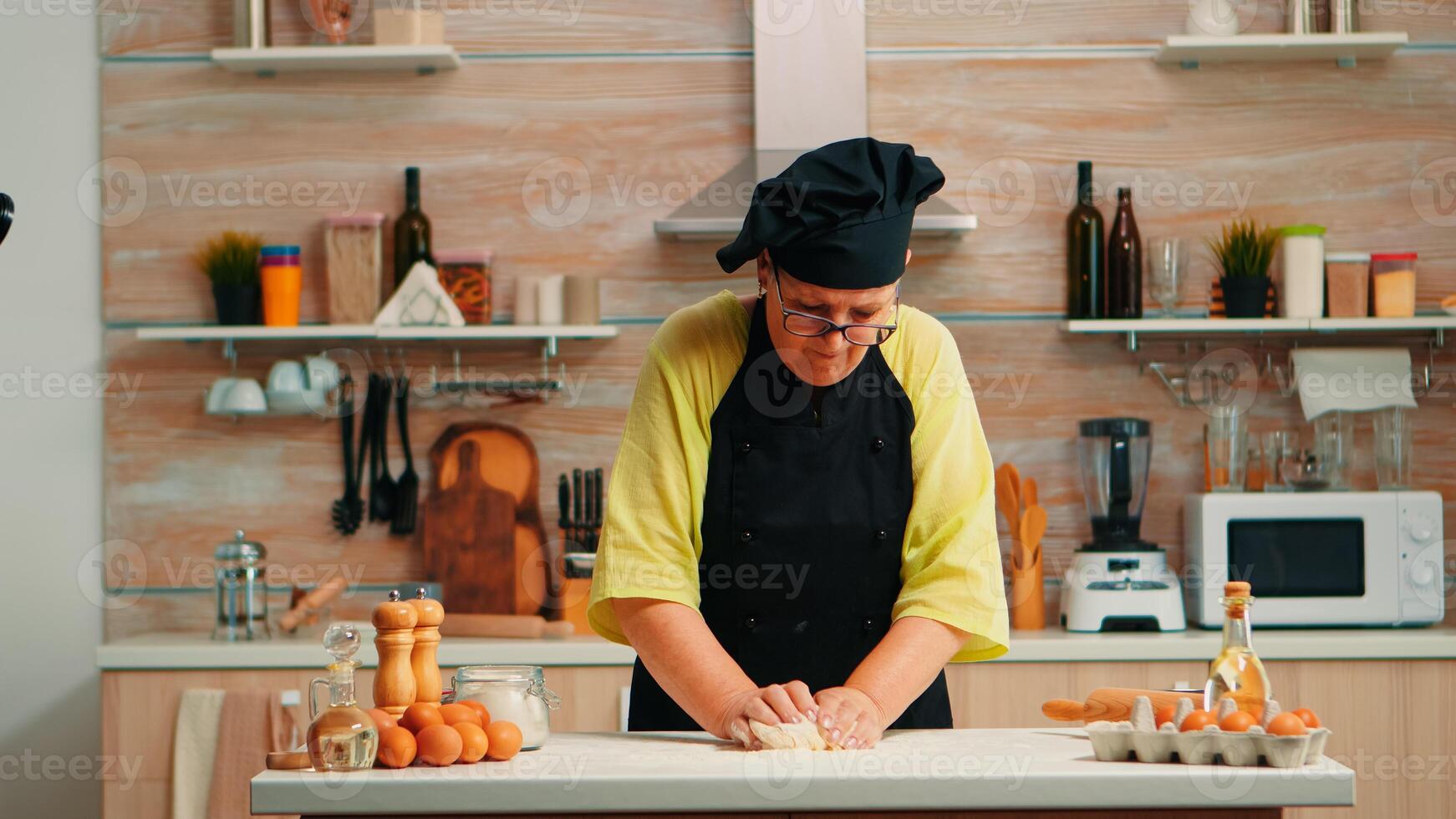 grootmoeder voorbereidingen treffen tarwe eigengemaakt brood vervelend chef bot. gepensioneerd ouderen bakker met bot menging ingrediënten met tarwe meel kneden deeg voor bakken eigengemaakt taart en brood foto