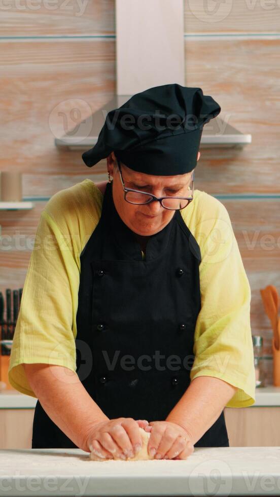 grootmoeder voorbereidingen treffen tarwe eigengemaakt brood vervelend chef bot. gepensioneerd ouderen bakker met bot menging ingrediënten met tarwe meel kneden deeg voor bakken eigengemaakt taart en brood foto