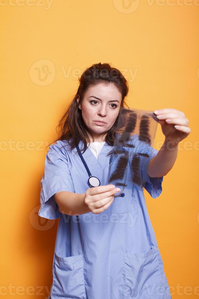 portret van medisch assistent tonen röntgenfoto beeld naar camera in studio. gezondheidszorg specialist vervelend uniform en stethoscoop terwijl analyseren ct scannen resultaten naar vind diagnose. foto
