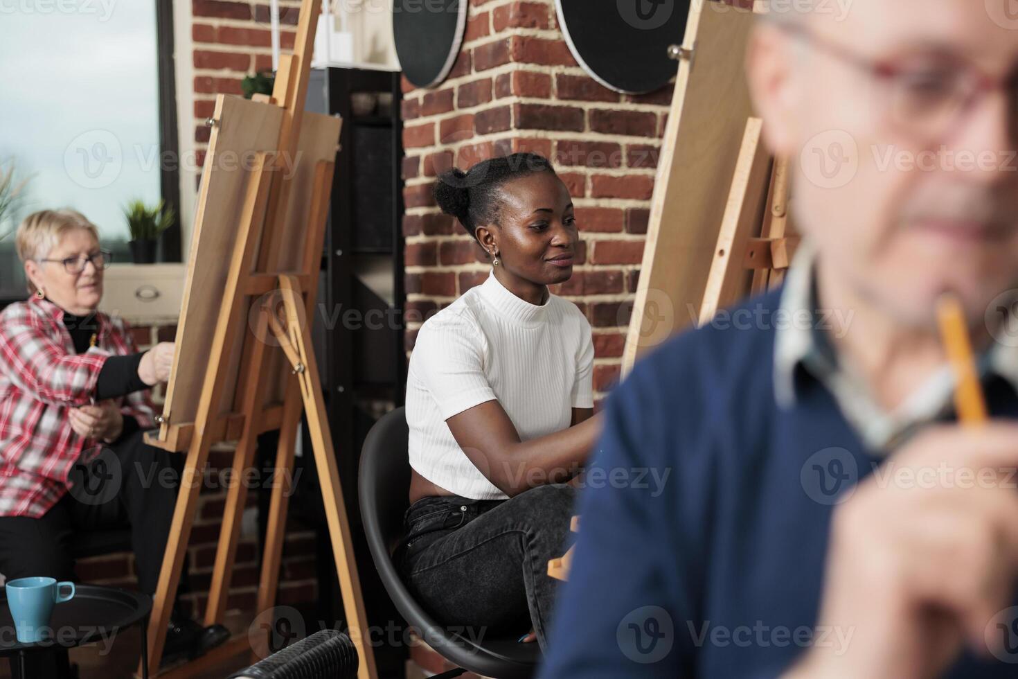 verschillend mensen van verschillend leeftijden aan het leren naar trek samen gedurende groep kunsten klas. glimlachen Afrikaanse Amerikaans millennial meisje tekening Aan canvas, krijgen creatief met familie en vrienden in kunst studio foto