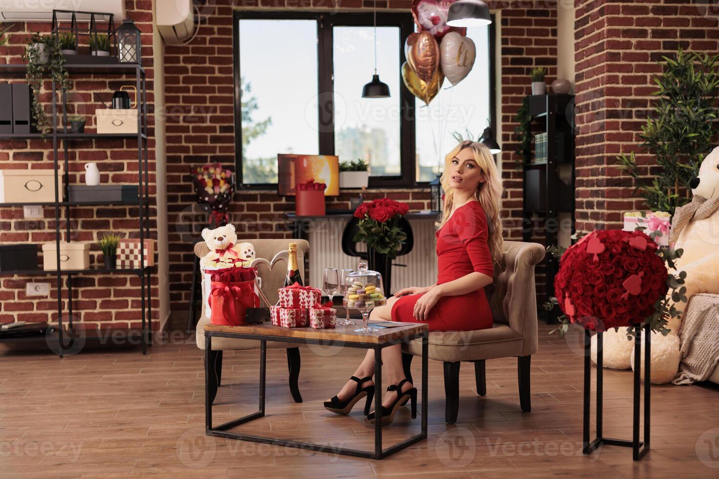 vrouw zittend in leven kamer gevulde met romantisch presenteert, ontvangen Valentijn s dag cadeaus van vriendje gedurende liefde vakantie. schattig blond vrouw in rood elegant jurk genieten van februari 14 verrassingen foto