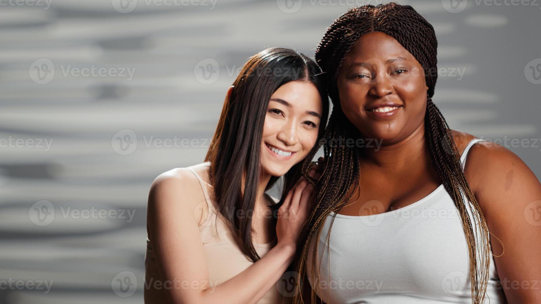 gelukkig interraciaal Dames lachend Bij camera en knuffelen, genieten van vriendschap en uitdrukken lichaam positiviteit. jong Dames gevoel zelfverzekerd en mooi, mager en golvend lichaam soorten. foto