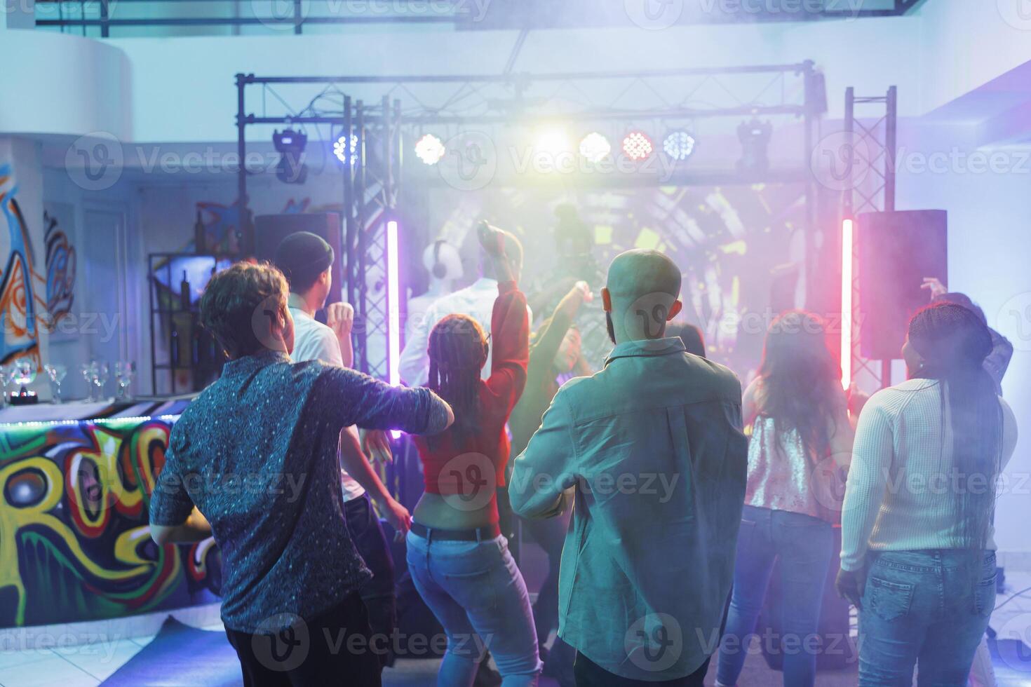 mensen feesten en hebben pret Aan dansvloer verlichte met schijnwerpers Bij discotheek. jong verschillend mannen en Dames dansen en jumping in druk nachtclub vol van clubbezoekers foto