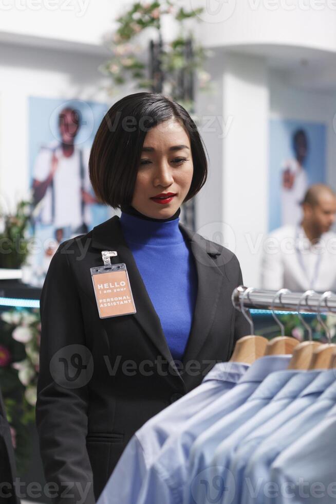 winkel Aziatisch vrouw werknemer onderzoeken overhemden Aan rek, organiserende handelswaar en beheren voorraad. boodschappen doen winkelcentrum kleding op te slaan verkoper controle hangende kleding in voorraad foto