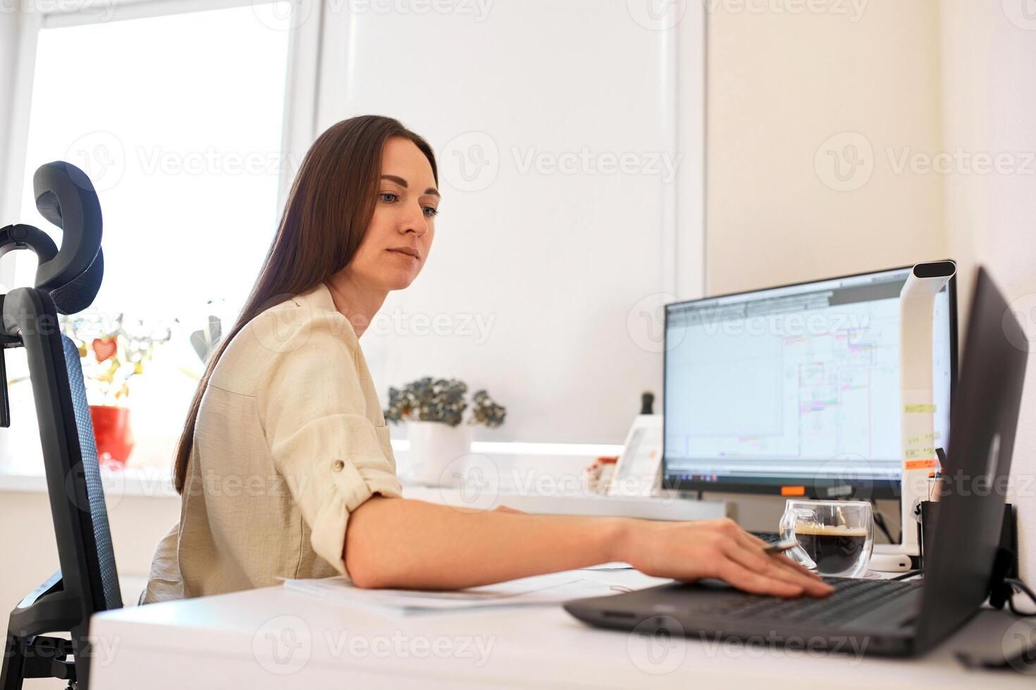 portret van een afgelegen arbeider. een volwassen vrouw zit Bij een tafel in voorkant van een computer en trekt omhoog een duur schatting. zelfverzekerd jong dame freelancer werken van huis. foto