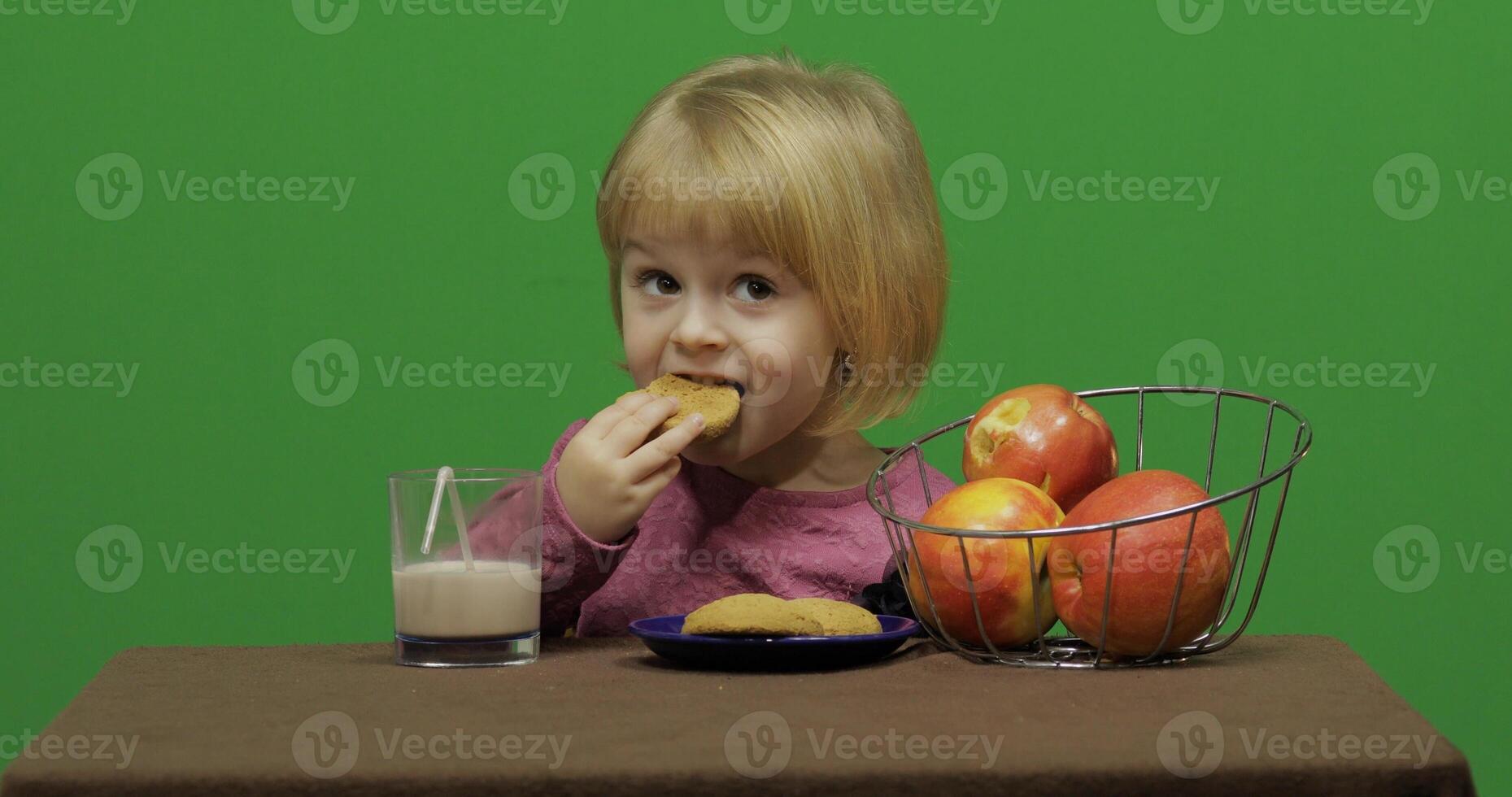 meisje zittend Bij de tafel met appels, cacao en aan het eten koekjes. chroma sleutel foto