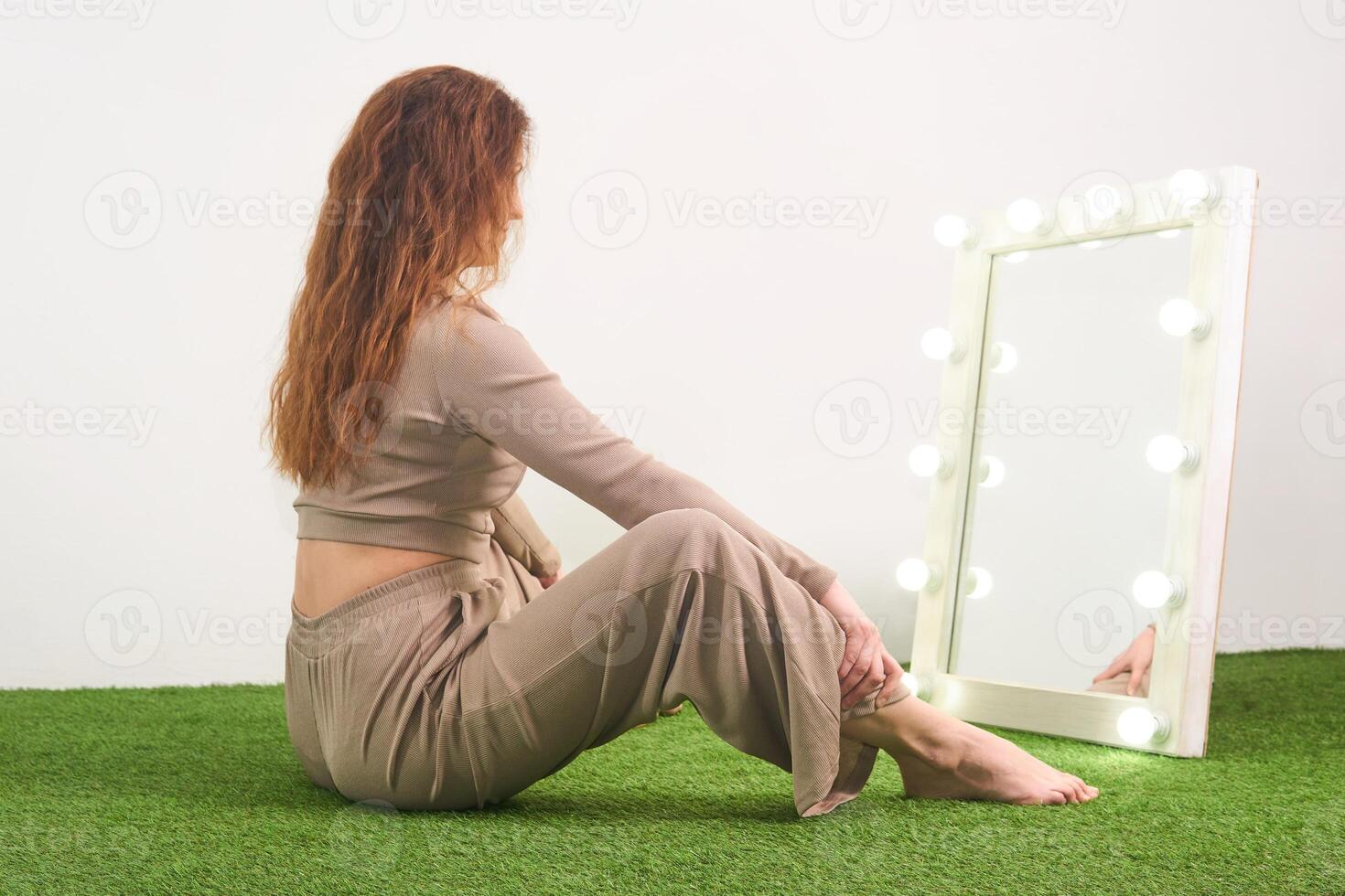 vrouw looks in de spiegel voor dressing kamer met verlicht, zittend Aan de verdieping in de studio foto