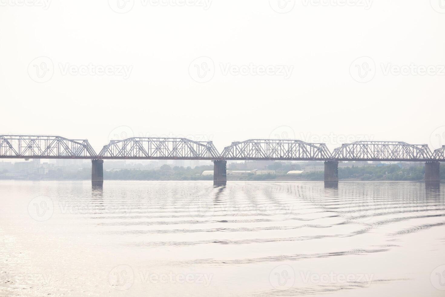 spoorweg brug over- een breed rivier- en de silhouet van een ver weg stad achter het in de ochtend- mist foto