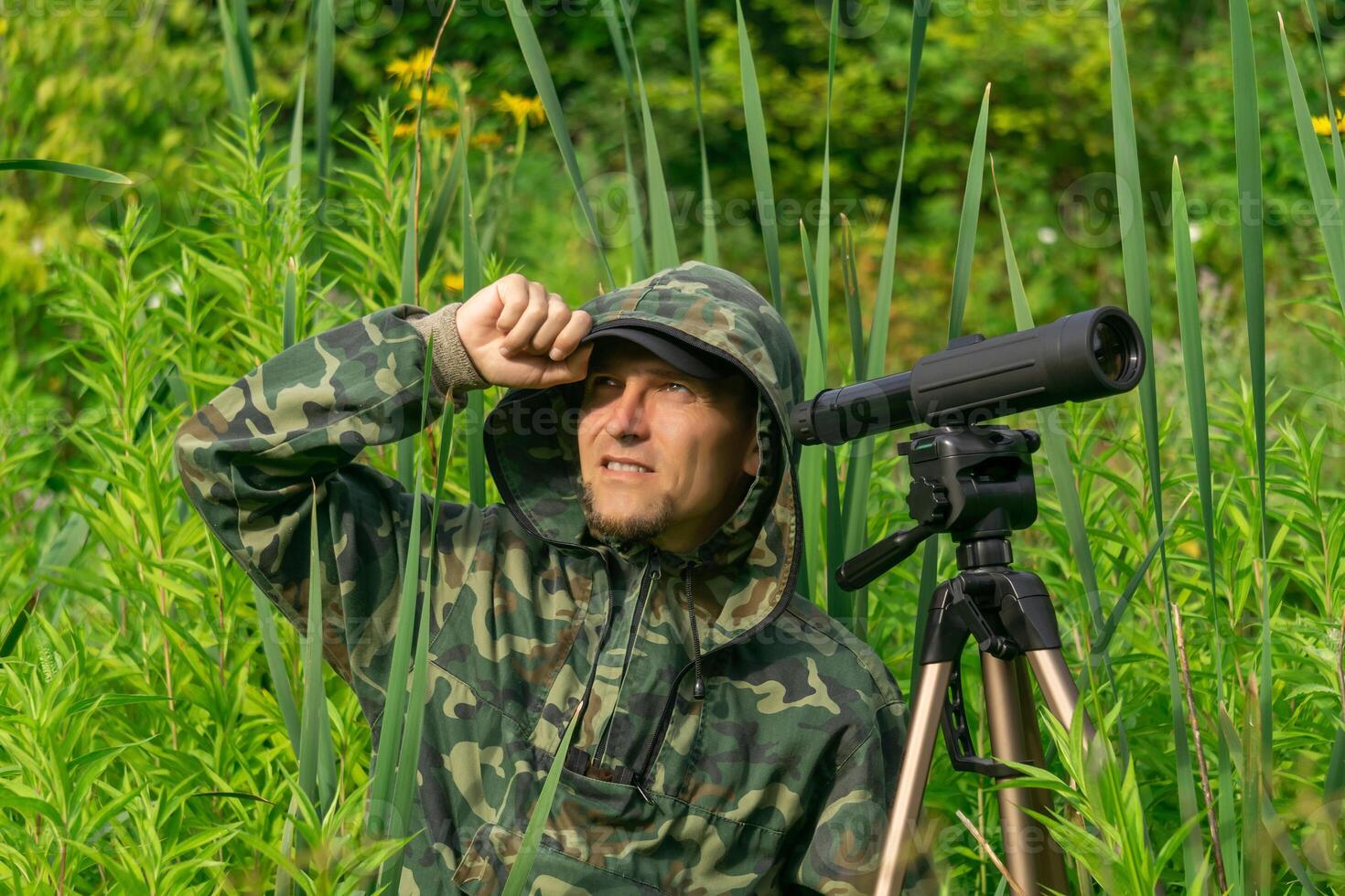 Mens vogelaar maakt veld- observatie met een spotten strekking tussen de struikgewas in een rivier- vallei foto