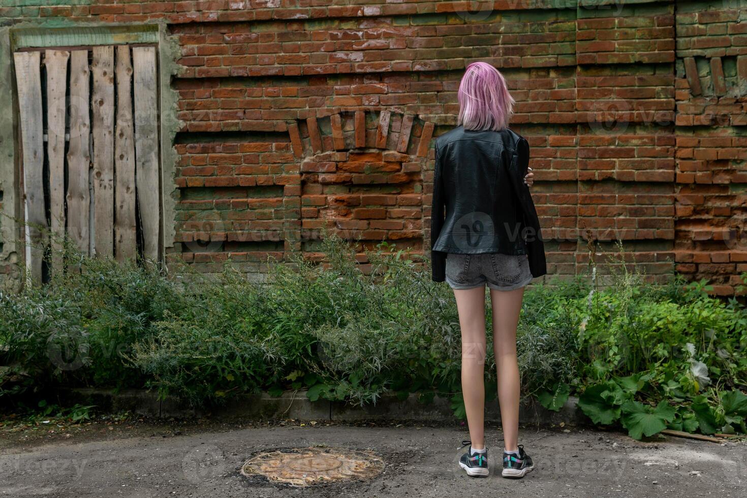 tiener- meisje staand alleen met haar terug naar de kijker tegen de achtergrond van een oud muur foto